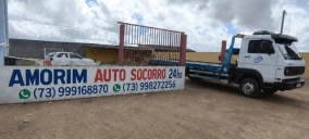 Guincho plataforma estacionado em Mucuri, com veículo visível ao fundo e placa de identificação da empresa.