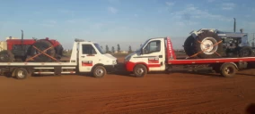 Dois guinchos de plataforma transportando tratores, um vermelho e um azul, em um terreno de terra em Nova Andradina.