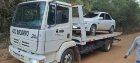 Guincho plataforma transportando um carro branco em estrada de terra em São Mateus.