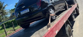 Guincho plataforma transportando um carro preto da marca Chevrolet em Conceição do Jacuíp.