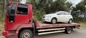 Guincho plataforma vermelho transportando um carro branco em Videira, estacionado na beira da estrada.