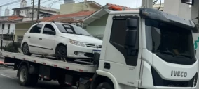 Guincho plataforma transportando um carro branco em Balneário Camboriú, estacionado em uma rua.