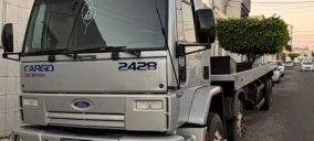Caminhão guincho Ford Cargo 2428 estacionado em rua de Lagarto, com carroceria plana e vegetação na caçamba.