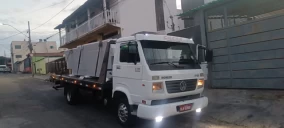Guincho plataforma branco estacionado em rua de Contagem, transportando materiais em sua caçamba.