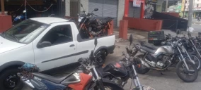 Caminhonete branca estacionada em Santo André, com motos na caçamba e outras motos ao redor.