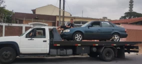 Guincho plataforma branco transportando um carro azul em Ubatuba.
