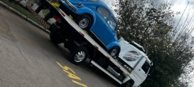 Guincho plataforma transportando um carro azul em Bauru, estacionado em uma rua com sinalização no chão.