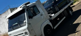 Guincho plataforma branco transportando um carro preto em Bauru, estacionado em uma rua.