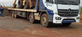 Guincho plataforma em Campo Grande, transportando uma máquina amarela, estacionado em área de terra.
