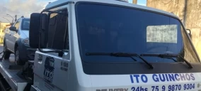 Guincho plataforma transportando um veículo cinza em Valença, com parte do caminhão visível e detalhes da cabine.