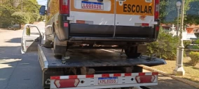 Guincho plataforma transportando uma van escolar em Carmo, com parte da rua visível ao fundo.