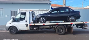 Guincho plataforma branco transportando um carro preto em Piraju, estacionado em uma rua residencial.