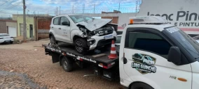 Guincho plataforma transportando um veículo branco batido em Juazeiro do Norte, com cones de sinalização visíveis.