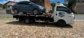 Guincho plataforma transportando um carro azul em Juazeiro do Norte, estacionado em área de pedras.