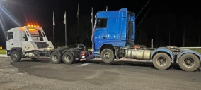 Guincho tipo plataforma em Cascavel, transportando caminhão azul estacionado à noite.