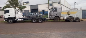 Guincho tipo plataforma transportando caminhão cinza em Ibema, estacionado em via pública.
