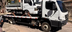 Guincho plataforma transportando um caminhão branco em Paracambi, com veículo amarrado e estacionado na rua.