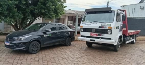 Guincho plataforma branco estacionado ao lado de um carro preto em Carazinho.