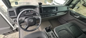 Interior de um caminhão guincho, com volante, painel e assentos visíveis, sem detalhes do veículo transportado.