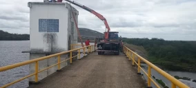 Guincho com braço articulado em Capim Grosso, operando próximo a uma estrutura sobre um corpo d'água.