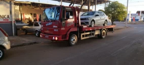 Guincho plataforma vermelho transportando um carro prata em Córrego Danta, estacionado em uma rua.