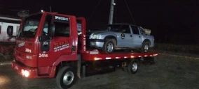 Guincho plataforma vermelho transportando um veículo prata em Córrego Danta, à noite.