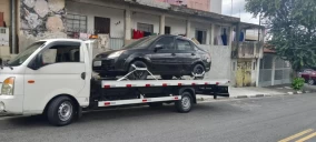 Guincho plataforma branco transportando um carro preto em Hortolândia, estacionado em uma rua residencial.
