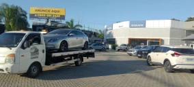 Guincho plataforma transportando um veículo sedan prata em Hortolândia, estacionado em área de concessionária.