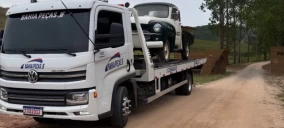 Guincho plataforma transportando um carro antigo verde em estrada de terra em Juiz de Fora.